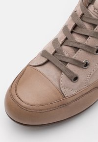 Brown leather sneaker with suede upper, round toe, and textured laces. Metal eyelets and stitched accents provide durability and detail.