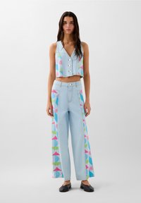Jasnoniebieski denimowy crop top z guzikami i kolorowymi geometrycznymi wzorami. Pasujące szerokie spodnie mają podobne wzory po bokach.