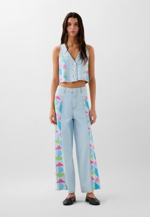 Cropped top in denim azzurro con bottoni e motivi geometrici colorati. I pantaloni a gamba larga coordinati presentano design simili sui lati.