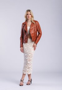 Bruine leren motorjack, witte cropped top, crèmekleurige kanten midi-jurk met bloemenpatronen, zwarte strappy hoge hakken sandalen.
