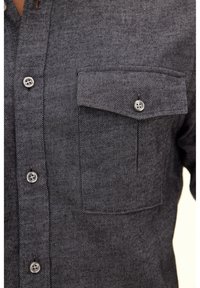 Camicia button-up grigia scura realizzata in tessuto strutturato, con una singola tasca sul petto, cuciture in vista e bottoni metallici rotondi.