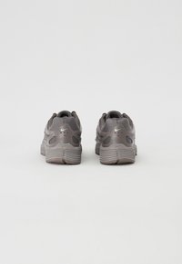 Baskets de sport grises avec une tige en maille texturée, semelle en caoutchouc contrastante et logo Nike visible. Présente un talon arrondi et des accents renforcés.