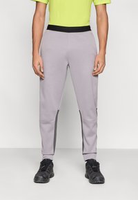 Ανοιχτό γκρι παντελόνι jogger από φλις με μαύρη ζώνη μέσης και γκρι πλαϊνές λωρίδες. Διαθέτει γραμμή που στενεύει προς τα κάτω και ελάχιστες ραφές.