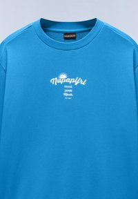 Sweat-shirt bleu vif à col rond avec texte blanc « Napapijri Make Your Mark Est. 1987 » et motif soleil centré sur la poitrine.