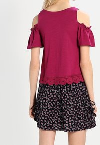 Top burdeos con hombros descubiertos y mangas con volantes, ribete de encaje en el dobladillo; combinado con una falda negra con un estampado floral rosa y cordones ajustables.