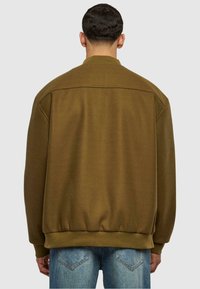 Brun genser med en avslappet passform, ribbet krage og mansjetter. Myk tekstur og elastisk kant. Brukt over lyseblå jeans.