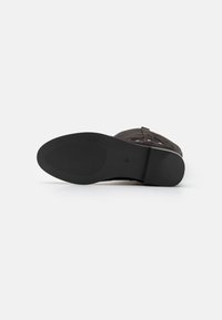 Suela de goma negra de una bota con un dibujo en la suela. Parte superior de textil gris con una correa que presenta tachuelas plateadas. Talla marcada como 37.