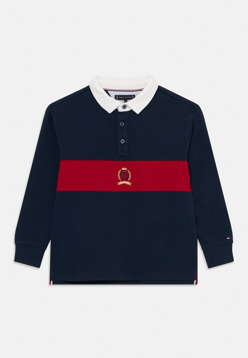 Polo de manga longa azul-marinho com colarinho branco, faixa horizontal vermelha e detalhe emblema dourado. Possui uma pala de três botões. Material em algodão.