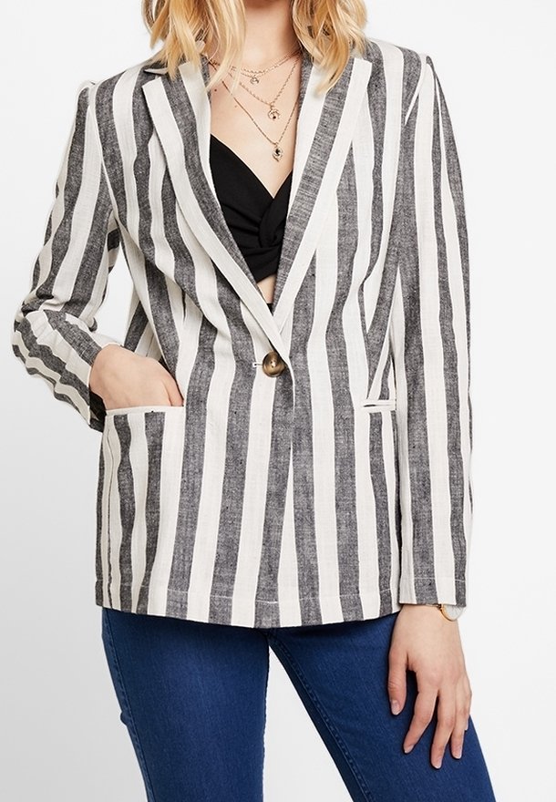 Femme portant un blazer rayé vertical noir et blanc par-dessus un haut noir et un jean bleu, avec une main dans la poche du blazer.