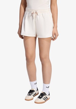 Donna che indossa pantaloncini bianchi con vita elasticizzata e coulisse frontale, calzini bianchi alla caviglia e scarpe da ginnastica beige con strisce nere.