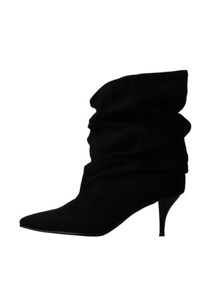 Bottine en daim noir ample avec bout pointu et petit talon fin sur fond blanc.