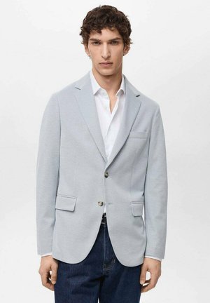 Blazer bleu clair en tissu doux, présentant un design à un seul boutonnage, des revers en pointe, des poches frontales et deux boutons. Assorti avec une chemise blanche.