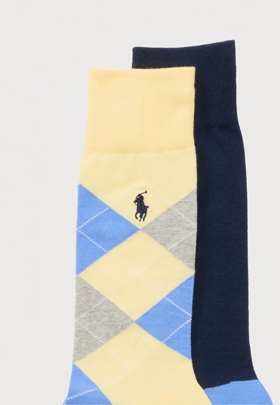 Ζευγάρι κάλτσες πλήρους μήκους, η μία μονόχρωμη σε ναυτικό μπλε, η άλλη κίτρινη με μοτίβο αργκλάι σε μπλε, γκρι και κίτρινο και κεντημένο λογότυπο.
