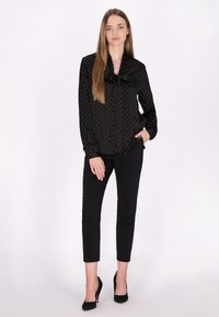 Bluză neagră cu buline albe, fundiță la guler, mâneci lungi; asortată cu pantaloni negri skinny și tocuri negre înalte.