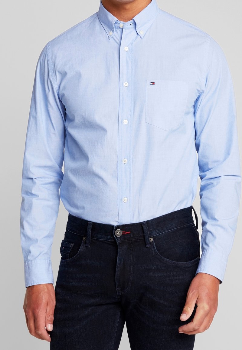 Helles blaues Baumwollhemd mit Knöpfen, einer Tasche auf der linken Seite und weißen Knöpfen, kombiniert mit dunkelblauen Jeans.