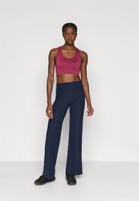 Ribbed navy flared pantsit yhdistettynä tiukkaan burgundin väriseen urheilurintsikkaan. Asusteessa on pehmeät tekstuurit ja saumatonta muotoilua. Mustat urheilukengät.