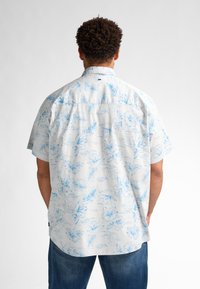 Camicetta a maniche corte con un motivo floreale azzurro su sfondo bianco, dotata di colletto a punta e vestibilità rilassata.