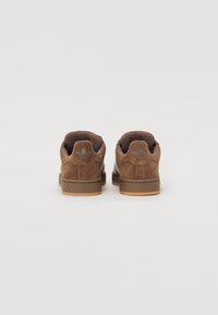 Brown suede sneakers with a textured finish, featuring a gum sole and embossed logo at the back, designed for casual wear.