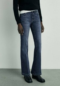 Tmavé denimové rozšířené džíny s středně vysokým pasem, které mají klasický pětikapsový design a prošití na švech.