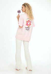 T-shirt oversized rose avec un graphique de fleur coloré et du texte au dos, associé à un pantalon évasé en côte blanc.