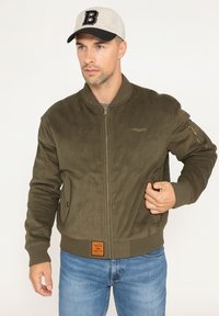 Veste bomber en velours côtelé olive avec col et poignets côtelés, fermeture éclair et poches latérales ; présente un patch en cuir à l'ourlet.
