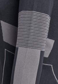 Sweter dziany w ciemnoszarym kolorze, z jasnoszarymi pionowymi paskami i geometrycznymi wzorami na rękawach. Widoczna tekstura tkaniny.