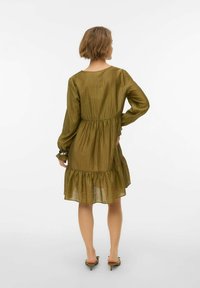 Oliiviroheline pikkade varrukatega kleit, millel on kihiline seelik ja volangidega mansetid. Valmistatud kergest, tekstuuriga kangast, langeb üle põlve.