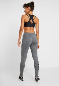 Svart sport-bh med korskryssade axelremmar, tillsammans med grå leggings i en texturerad tyg och svarta chevron-detajer på sidan.