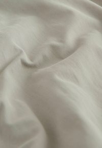 Miękki, beżowy materiał z delikatnymi fałdami i gładką, lekko teksturowaną powierzchnią.