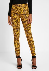 Jeans ajustados con patrón de serpiente en amarillo y negro, de cintura media, con estilo de cinco bolsillos y cierre de botón metálico.