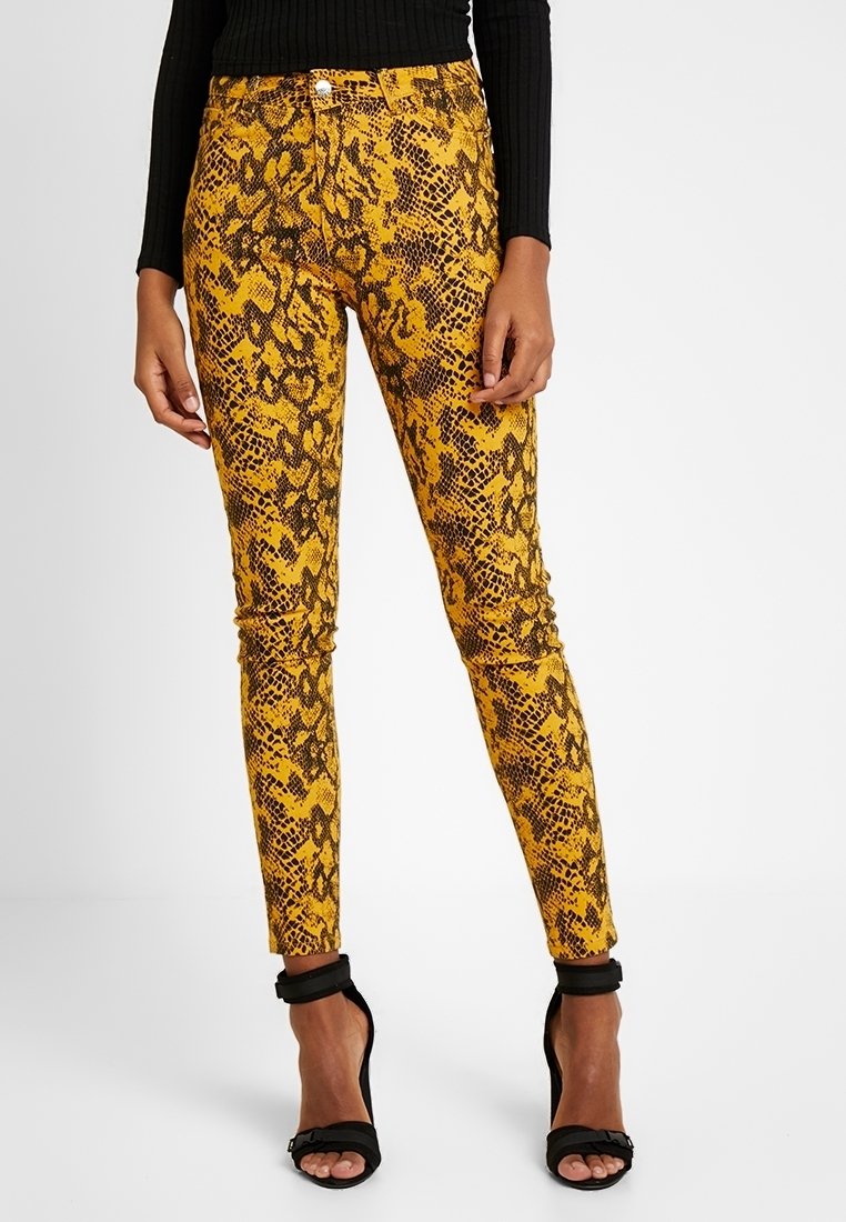 Jeans ajustados con patrón de serpiente en amarillo y negro, de cintura media, con estilo de cinco bolsillos y cierre de botón metálico.