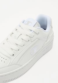 Baskets blanches en cuir lisse avec une semelle en caoutchouc texturée. Présente un logo brodé, un bout rond et un design à lacets.
