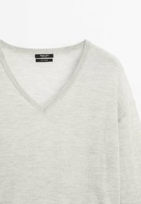 Lichtgrijze cashmere sweater met een V-halsontwerp, zachte textuur en subtiele ribbelranden. Etiket leest "100% Cashmere" en merknamen.