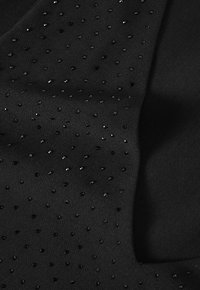 Črno blago s fino teksturo je posuto z razpršenimi, sijočimi črnimi sequini, ki ustvarjajo subtilen vzorec na gladki podlagi.