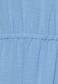 Tecido azul claro com uma textura suave, apresentando uma costura franzida ao centro. O material é respirável e ligeiramente amassado.