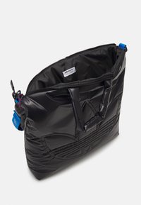 Sac cabas en nylon noir avec un design matelassé, doté de deux poignées et d'un accent bleu. Ouverture zippée révélant un intérieur spacieux.