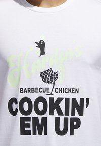 Camiseta blanca de manga corta con texto gráfico en negro y verde claro: "Harden's Barbecue Chicken Cookin' Em Up" acompañado de una ilustración estilizada de un pollo.