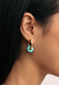 Guldörhänge med en turkos rund pärla med svart marmorerad yta, bärs i örat. Slät textur och rundad design.