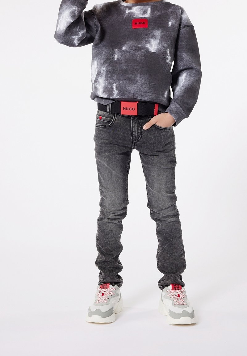 Sweat-shirt tie-dye noir et gris avec un patch logo rouge, jean skinny gris avec des accents foncés, et baskets chunky grises avec des lacets roses.