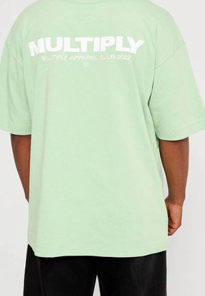 Light green oversized t-shirt made of cotton, featuring bold white text "MULTIPLY" and "MULTIPLY APPAREL CLUB 2022" on the back.