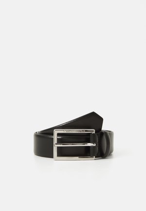 Cintura in pelle nera arrotolata con una lucente fibbia rettangolare argento incisa con un nome di marca su uno sfondo bianco.