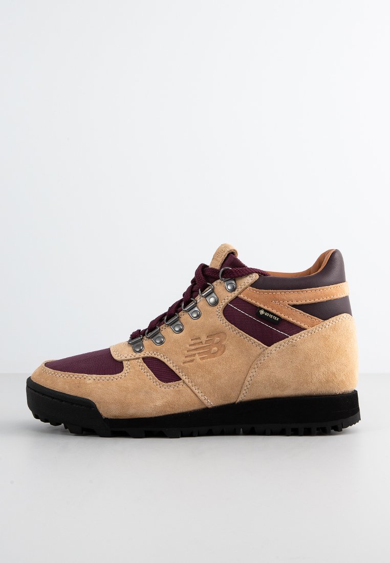 Hochschuh-Wanderschuhe mit einem Obermaterial aus beigem Wildleder, burgunderfarbenen Akzenten, Metallösen und einer schwarzen Gummisohle.