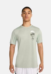 Camiseta de Nike de color verde claro y manga corta, con un estampado gráfico de un balón de baloncesto y una mano en el lado izquierdo del pecho, confeccionada en un material suave y transpirable.