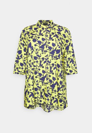 Lange gele blouse met paars bloemmotief, driekwart mouwen, knoopsluiting aan de voorkant en een klassieke kraag.