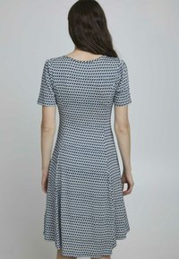 Kortärmad klänning med en figurnära överdel och utsvängd kjol, tillverkad av tyg med ett blått och vitt geometriskt mönster.