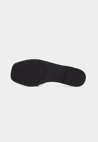 Semelle plate noire avec une surface texturée à l'avant et un talon lisse, portant une discrète marque en relief "ALDO".