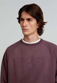 Felpa viola con collo a costine e maniche raglan. Presenta il logo ricamato "SCALPERS" nello stesso colore sul davanti.