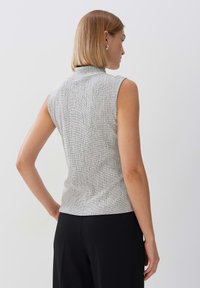 Mouwloze top met hoge hals in een zwart-wit gestructureerd patroon, aansluitend ontwerp en subtiele stretchstof, gecombineerd met zwarte trousers.