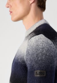 Strickpullover mit einem Farbverlaufsmuster, das von Dunkelblau zu Hellgrau übergeht. Er verfügt über einen runden Halsausschnitt und einen strukturierten Stoff. Enthält ein Logopatch.