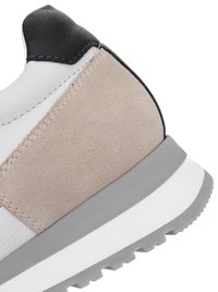 Nahaufnahme der Ferse eines grauen, weißen und schwarzen Sneakers mit Wildleder- und Ledertexturen sowie einer dicken Gummisohle mit Profilmuster.